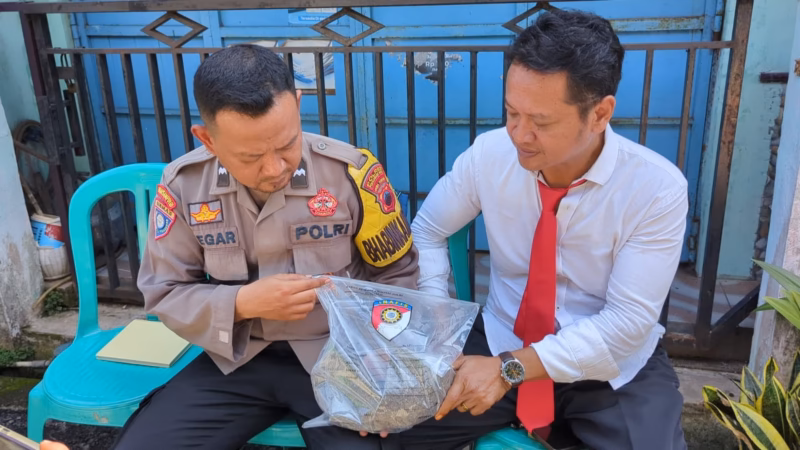 Dua anggota polisi mengamankan barang bukti cobek batu dari dalam rumah duka yang digunakan pelaku untuk menganiaya ibu kandungnya hingga meninggal dunia, Senin (11/5/26).