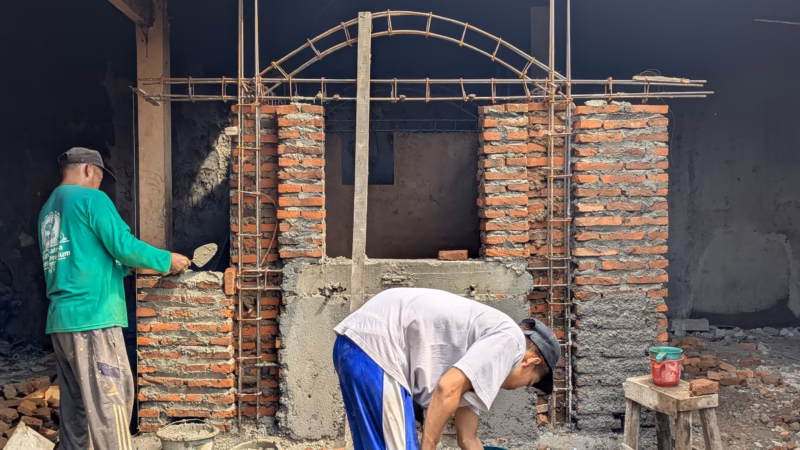 Dua pekerja sedang membangun tungku bakar tanah liat yang dilapisi dinding batu bata di lokasi TPS3R Kelurahan Medono, Minggu (17/5/26).