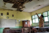 Seorang guru menunjukkan ruangan kelas yang mengalami kerusakan berat, Selasa (28/7/26). Foto : Ilustrasi AI