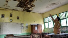 Seorang guru menunjukkan ruangan kelas yang mengalami kerusakan berat, Selasa (28/7/26). Foto : Ilustrasi AI